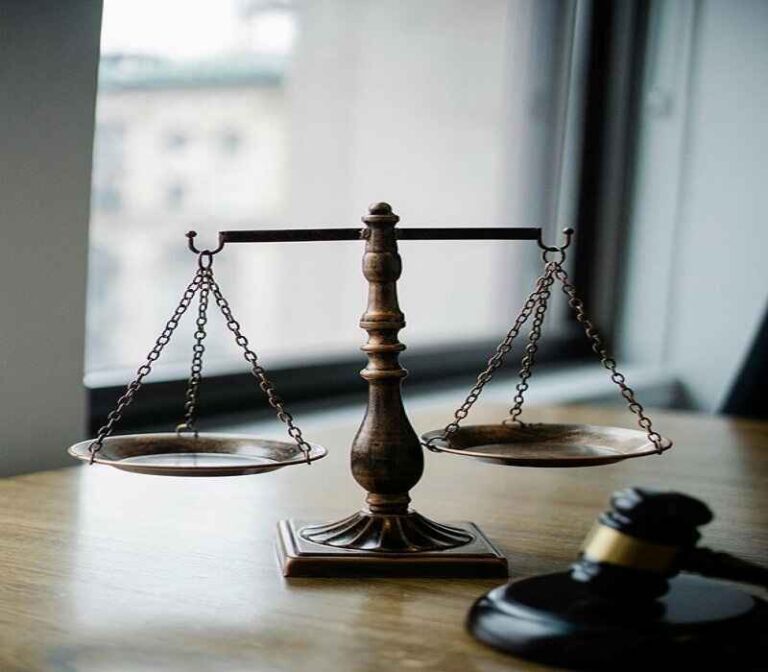 Scales of justice on a wooden desk with a gavel nearby, symbolizing law and fairness.